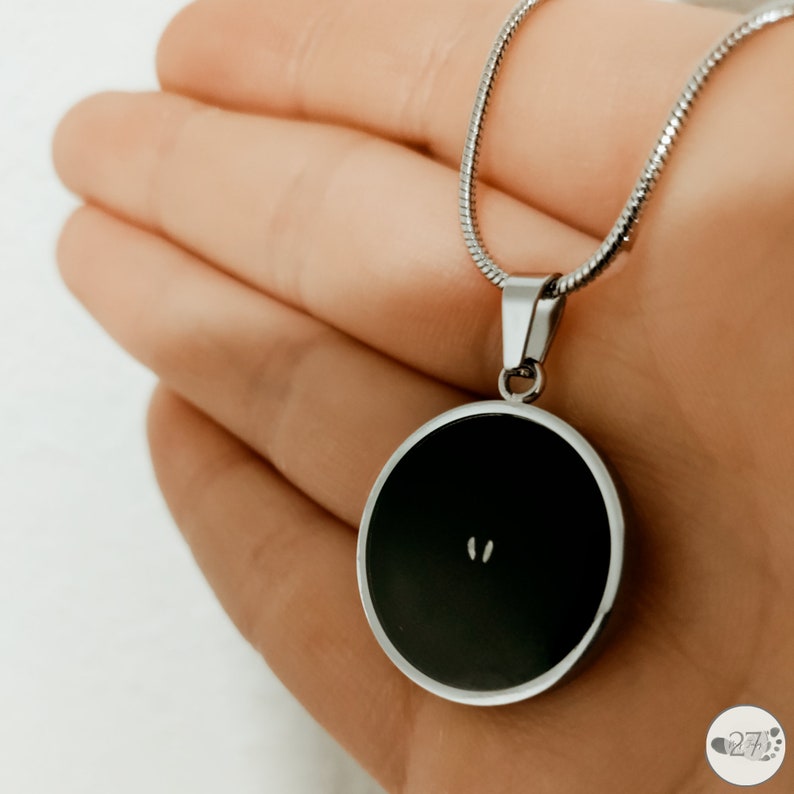 May include: A silver chain necklace with a round black pendant. The pendant has a small silver design in the center.