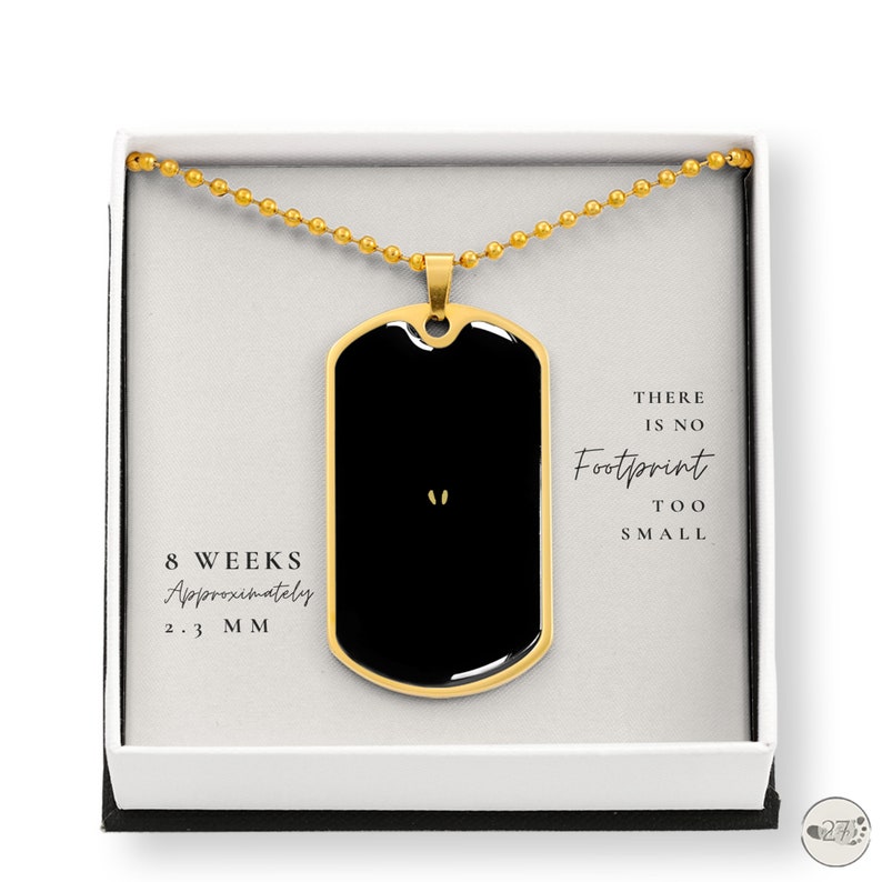 May include: Gold necklace with a black dog tag pendant. The dog tag has a small footprint image and the text "There is no footprint too small". The necklace is in a white box with the text "8 weeks approximately 2.3 mm" on the bottom.