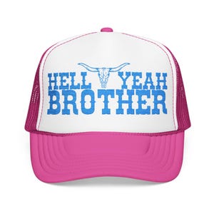 May include: A pink and white trucker hat with the text "HELL YEAH BROTHER" in blue, and a longhorn skull graphic. The hat has a pink brim and mesh back.
