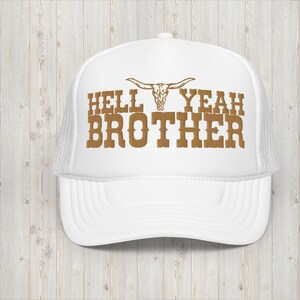 Könnte beinhalten: Weiße Trucker-Kappe mit einem braunen gestickten Design, das "Hell Yeah Brother" mit einem Bullenschädel über dem Text sagt.
