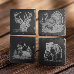 May include: Set of four black slate coasters with engraved images of a deer, a turkey, an elk, and a bear. The images are in a white color.