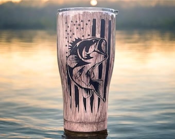 Könnte beinhalten: Ein Edelstahlbecher mit Holzmaserung. Das Design zeigt eine schwarze Grafik eines Fisches mit einer stilisierten amerikanischen Flagge. Der Becher ist für kalte und heiße Getränke konzipiert.