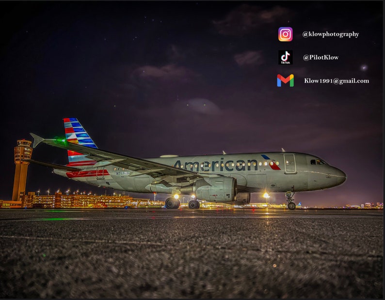 Może przedstawiać: Biały samolot American Airlines z czerwonymi, białymi i niebieskimi akcentami jest zaparkowany na pasie startowym w nocy. Samolot jest oświetlony światłami na pasie startowym i terminalem lotniska w tle. Niebo jest ciemne, a gwiazdy są widoczne.