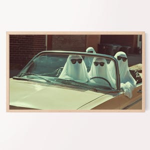 May include: A framed print featuring a vintage convertible car with four ghosts wearing sunglasses. The ghosts are draped in white sheets. The car is a light yellow color, and the background includes a brick building and trash cans.