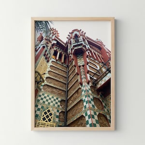 May include: A framed wall art print featuring a low-angle view of a building facade with red and brown stone walls, accented by decorative green and white checkered tile patterns, yellow window shutters, and intricate architectural details.