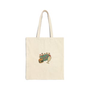 May include: Cream-colored tote bag with a retro diner-style graphic. The graphic features a burger, milkshake, and the text "Greasy Spoon Special" in a teal oval. The bag has two long handles.