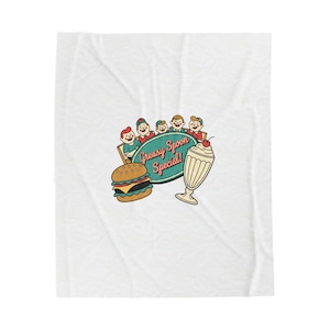 May include: White blanket featuring a retro diner design. The design includes a burger, milkshake, and a sign that reads "Greasy Spoon Special!" with cartoon characters. The color palette is primarily red, teal, and cream.
