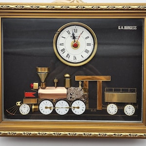 May include: A gold framed clock with a black background and a steam engine design. The clock face is white with black Roman numerals and a red second hand. The steam engine is made of metal and has a copper boiler. The clock is signed "G.A. Burgess".
