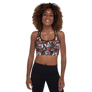 May include: Black sports bra with a repeating pattern of a cartoon dog wearing a bandana and playing a guitar. The dog is surrounded by red stars and the words "Rock" and "Just Rock".