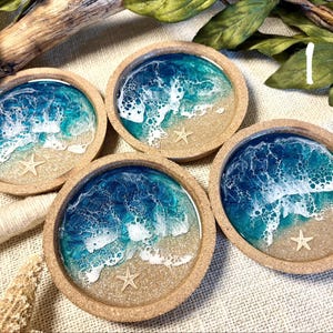 May include: Four circular coasters with a natural cork rim, featuring a resin art design that mimics a beach scene with blue and turquoise ocean waves, white sea foam, sandy beige shores, and a small embedded starfish in each piece.