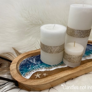 May include: Wooden tray with a resin ocean wave design and three white candles with gold glitter accents. The tray has a black metal handle.