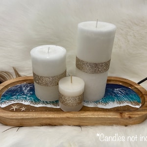 May include: A wooden tray with a resin ocean scene and three white candles with gold glitter accents. The tray has a black metal handle. *Candles not included*