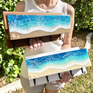 May include: Two wooden key racks with ocean-themed resin inserts. The top rack has two starfish and the bottom rack has a wave design. Both racks have five hooks.