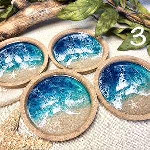 May include: Four circular coasters with a raised cork rim, each featuring a resin art design of a beach scene with blue and turquoise ocean waves, white sea foam, sandy shores, and a small embedded starfish in the center of each sandy area.