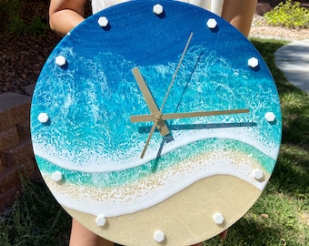 May include: A round clock with a blue and white ocean wave design. The clock face has white hexagon-shaped hour markers and gold hands.
