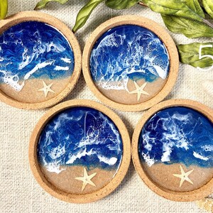 May include: Four circular coasters with a cork rim, each featuring a resin art design of a blue ocean with white sea foam waves crashing onto a sandy beach. A small, light-colored starfish is embedded in the sand section of each coaster.