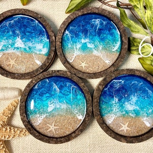 May include: Four circular coasters with dark brown cork frames. Each coaster features a resin ocean scene with a sandy beach, a small beige starfish, and swirling blue and turquoise water with white foam waves crashing against the shore.