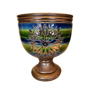 May include: A decorative ceramic bowl with a pedestal base. The bowl features a floral design in shades of green, blue, and gold. The rim and base have a bronze-like finish. The bowl is suitable for display or as a decorative accent.