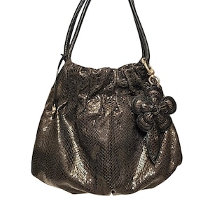 May include: A brown snakeskin handbag with a black flower charm. The bag has a gathered top and two black handles.