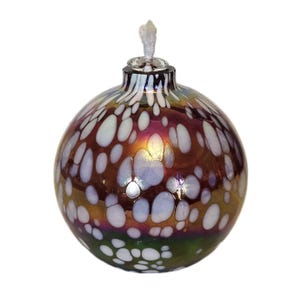 May include: A spherical glass oil lamp featuring an iridescent, multi-colored surface with a metallic sheen. The exterior is decorated with a pattern of opaque white, rounded spots of varying sizes. A clear glass neck holds a white fabric wick.