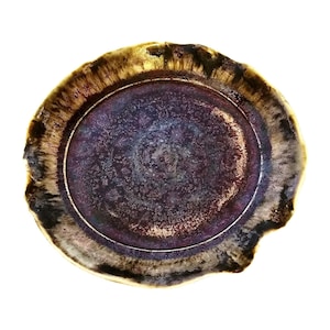 May include: A handcrafted ceramic plate with a unique, organic shape. The plate features a deep purple center with a textured surface, surrounded by a metallic gold and brown rim. The plate's irregular edge adds to its artistic appeal.