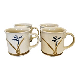 May include: Set of four ceramic mugs with a beige background and brown and blue floral designs. The mugs have a rounded shape and a handle.