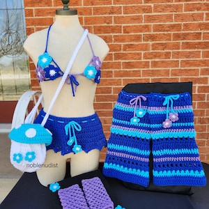 May include: A crochet outfit set in shades of blue, purple, and white, including a bikini top, skirt, and shorts. The set features flower accents and a mushroom-shaped purse. Also included are a pair of fingerless gloves.