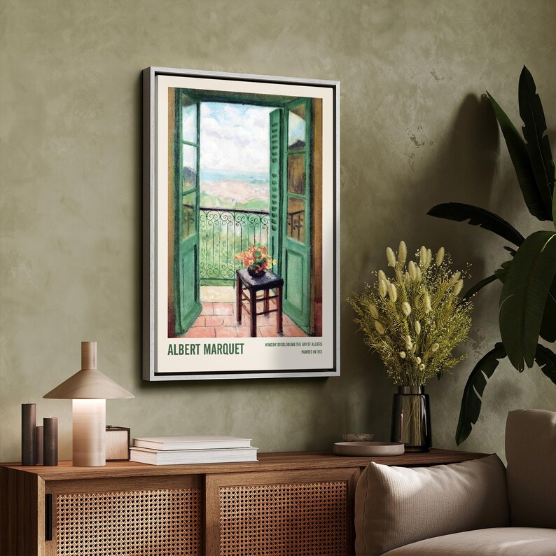 May include: A vintage poster featuring a painting of an open balcony door with a view of a cityscape. The door is green and the balcony is iron. A small table with a vase of flowers sits on the balcony. The poster is titled "ALBERT MARQUET" and includes the text "WINDOW LOOKING OUT ON THE BAY OF ALGIERS, PAINTED IN 1912."