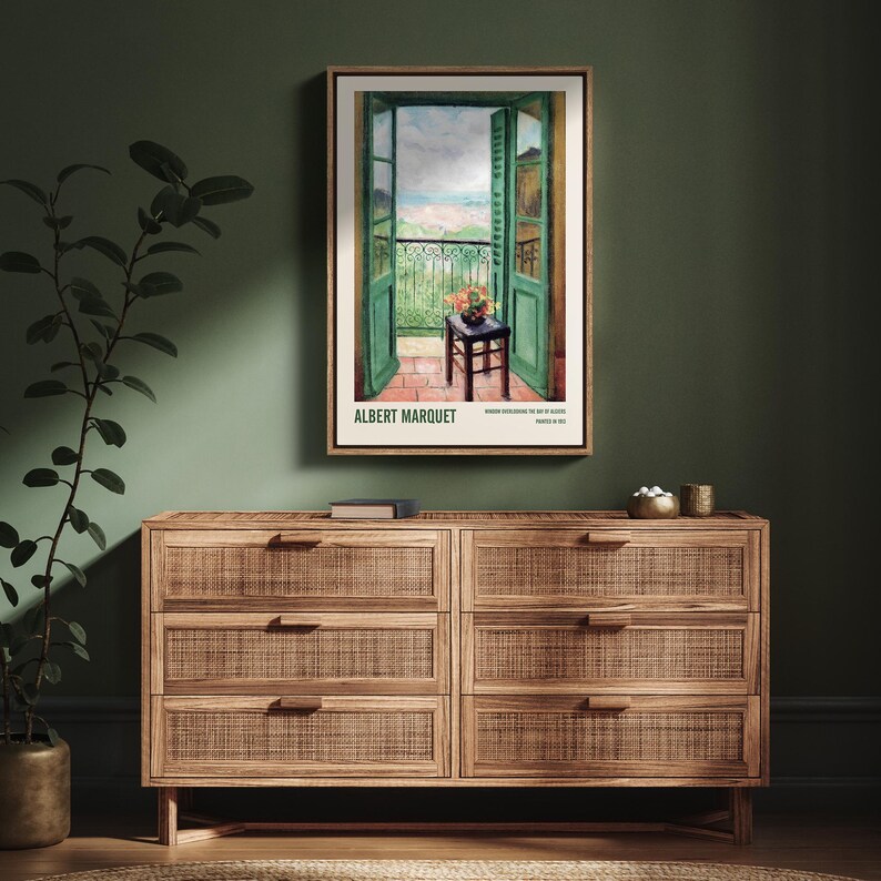 May include: A vintage poster featuring a painting of an open balcony door with a view of a seaside town. The poster is framed and has the artist's name, "ALBERT MARQUET", printed at the bottom.