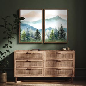 May include: Two framed watercolor landscape paintings depicting mountains and evergreen trees in shades of blue, green, and peach. Below, a wooden dresser with six drawers and woven rattan panels.