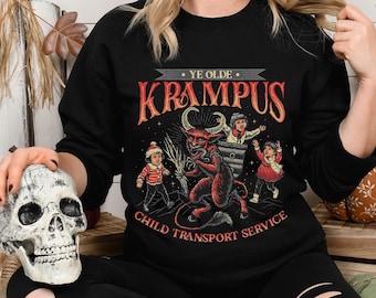 May include: Black sweatshirt with a vintage-style graphic featuring Krampus, a horned figure, and the text "Ye Olde Krampus Child Transport Service." The design includes children and a devilish character. The image also includes a decorative skull.