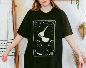 May include: Black t-shirt featuring a white graphic of a tarot card. The card is labelled "XVIII THE COLOR" and depicts a stylised image of a hair dye brush and bowl.
