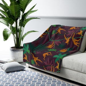 May include: A burgundy throw blanket with a repeating pattern of orange monkeys swinging from green vines and palm trees.