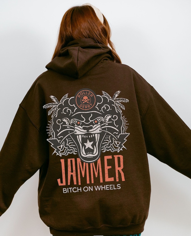 May include: Brown hoodie with a graphic print of a snarling panther with a star in its mouth. The graphic also includes palm trees and the text "Roller Derby" and "Jammer Bitch on Wheels".