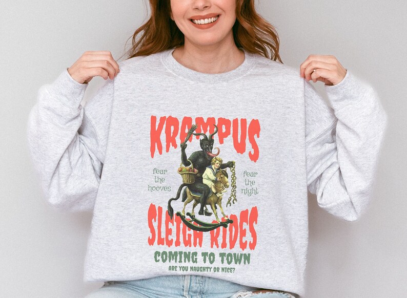 May include: Gray sweatshirt with a red graphic print of a Krampus figure riding a rocking horse with a child. The text reads "Krampus Sleigh Rides Coming to Town Are You Naughty or Nice?"