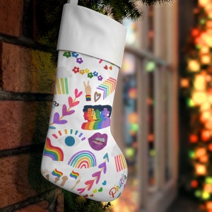Könnte beinhalten: Weißer Weihnachtssocken mit einem Regenbogen, einem Friedenszeichen und anderen bunten Designs. Der Socken trägt das Wort "Pride".