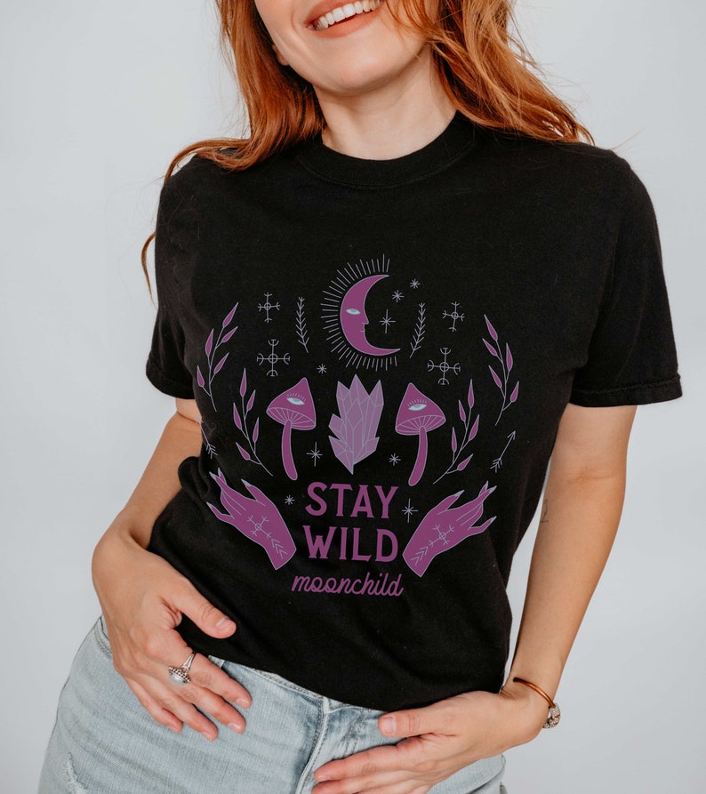 K&ouml;nnte beinhalten: Schwarzes T-Shirt mit einem lila und wei&szlig;en Grafikdesign mit Pilzen, einem Halbmond und dem Text "Stay Wild moonchild".