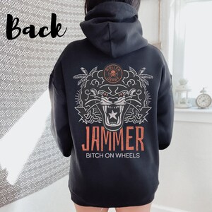May include: Black hoodie featuring a white graphic of a snarling panther with a star on its chest. The graphic also includes palm trees and the text "Roller Derby" and "Jammer Bitch on Wheels".