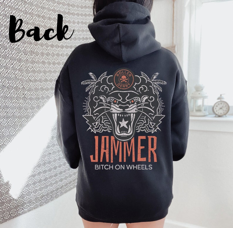 May include: Black hoodie featuring a white graphic of a snarling panther with a star on its chest. The graphic also includes palm trees and the text "Roller Derby" and "Jammer Bitch on Wheels".