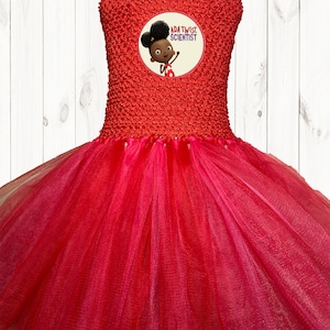 May include: A red tulle tutu dress with a red bodice featuring a circular patch with the text "Ada Twist, Scientist" and an illustration of a young girl with brown skin and curly black hair.