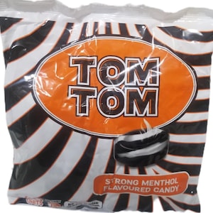 May include: A clear plastic bag of Tom Tom strong menthol flavored candy. The bag has a white and black striped pattern. The candy is in an orange oval with the words "TOM TOM" in white letters. A single candy is visible.