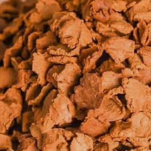 May include: Close-up of a pile of textured, light brown food pieces. The pieces have irregular shapes and a slightly rough surface, suggesting a crunchy texture. The color is a warm, inviting shade of brown.