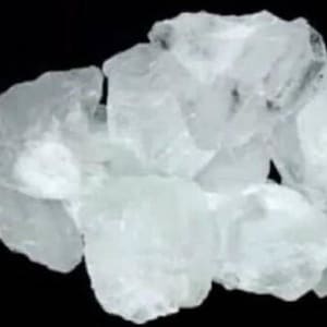 Peut inclure: Gros plan sur un amas de morceaux cristallins translucides sur fond noir. Les formes irrégulières et les facettes des cristaux reflètent la lumière, créant un effet scintillant. L'ensemble suggère un spécimen minéralogique ou géologique.