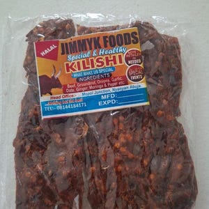Op de afbeelding: Een verpakking Jimmyk Foods Kilishi, een speciaal en gezond rundvleesproduct. Het etiket vermeldt ingrediënten zoals rundvlees, pinda, uien, knoflook, dadel, gember, moringa en peper. Het product zit in een transparante plastic verpakking.
