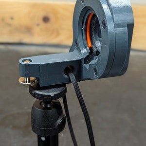Puede incluir: Un soporte de c&aacute;mara de impresi&oacute;n 3D gris con una perilla negra y un cable negro conectado a un tr&iacute;pode negro.