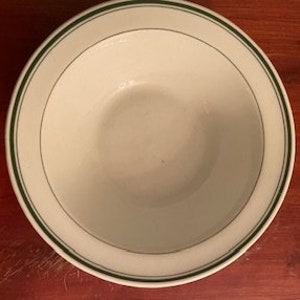 May include: White ceramic bowl with a green rim. The bowl has a simple design with two thin green lines around the edge.