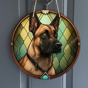 Puede incluir: Una ilustración redonda de estilo vitral de un perro belga Malinois marrón y negro con un fondo verde, amarillo y marrón. El perro está mirando hacia la derecha de la imagen. La imagen está enmarcada en un marco de madera marrón.