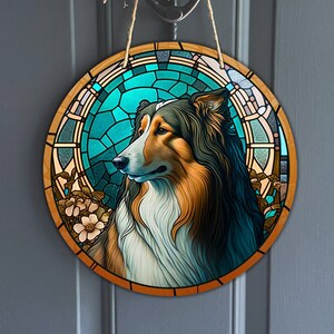 Op de afbeelding: Een rond houten bord met een glas-in-loodontwerp met een Collie-hond met bruine, witte en zwarte vacht. De hond wordt omringd door een blauw en groen glas-in-loodontwerp met bloemmotieven.
