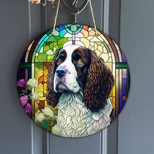 Könnte beinhalten: Ein rundes, farbenfrohes Buntglasdesign mit einem Springer Spaniel mit braunem und weißem Fell. Der Hund schaut nach rechts und hat eine braune Nase und braune Augen. Das Buntglasdesign ist von einem Blumenrand umgeben.