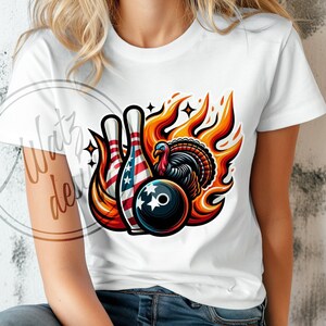 May include: A white t-shirt with a graphic design of a turkey, bowling pins, and a bowling ball. The bowling pins are decorated with the American flag. The turkey is surrounded by flames.